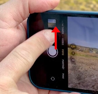 Prst přetahuje spoušť fotoaparátu iPhonu ve směru červené šipky.